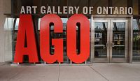 Photo of the large red AGO sign at the Art Gallery of Ontario entrance, showing the museum's front doors and surrounding area.