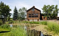 Exterior view of historic wooden winery building adjacent to a pond and landscaped grounds with trees and grasses.