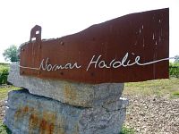 Rust-coloured metal sign reading “Norman Hardie” mounted on stone base