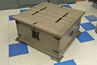 Square wooden coffee table trunk with grey-washed finish, metal hinges, side handles, and central lock
