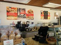 Interior counter and kitchen area of Pasta Shelf showing bread set and menu posters.