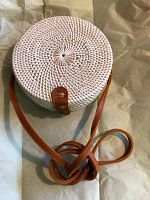 Photo of round white wicker clam-shell purse with brown leather strap and clasp, showing woven design and shape.