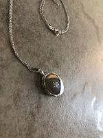 Close-up of sterling silver oval locket and chain laid flat on surface, showing star engraving on locket face and chain details