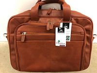 Front view of caramel brown leather laptop case with multiple zippered compartments and attached Mancini Colombian Collection tags.