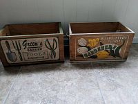 Two wooden decorative garden boxes side by side on tiled floor with garden-themed prints.