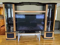 Front view of the entertainment center with glass display cabinets closed and Panasonic TV centered in middle compartment