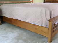 Side view showing wooden bed frame with light beige king size bedspread with circular pattern covering the mattress.