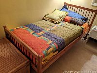Wooden twin bed with multi-colored patchwork quilt and pillows in a bedroom setting