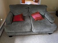 Front view of gray fabric love seat with two decorative red and pink pillows