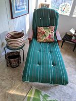 Front view of redwood chaise lounge with green cushion and floral pillow on tiled floor near basket and small stool.