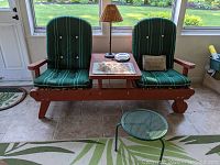 Front view of redwood glider bench with center table, cushions, pillow, lamp, tray and dish on tiled floor.
