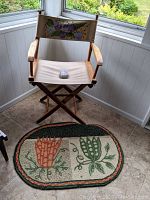 Director's chair with beige canvas seat and small floral rug on tiled floor near a window.