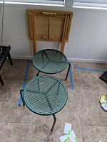 Two small round green metal tables with mesh tops and three legs each, viewed from above and side.