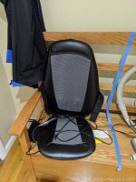 Black electric chair cushion placed on wooden chair with attached wires and straps for securing cushion.