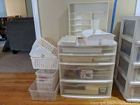 Full view of the plastic storage cabinet with multiple drawers and the assortment of various white plastic drawer and closet organizers stacked on top and next to it.