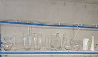 Wide view of various clear glass and one white ceramic vases on two shelves, assorted shapes and sizes