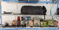 Shelf with black sleeping bag, various lanterns including Coleman lamps, and boxed camping equipment.