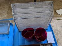 Four metal mesh desk organizers including a multi-tier file sorter and a tray, plus two red plastic pen holders with compartments arranged for photo.