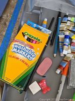 Photo showing box of Crayola washable markers, black pencils, eraser, and several small tubes of paint laid out on a tabletop