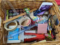 Photo of a basket containing various school supplies such as rolls of tape, star stickers, scissors, sticky notes, rulers, pens, notebooks and other small office tools.