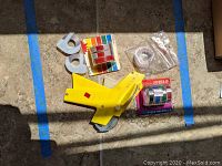 Photo showing yellow handheld label gun and various tape rolls on a tile floor.