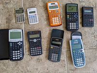 Wide photo showing all 10 calculators arranged on a stone surface, varying from basic to scientific models in various colors.