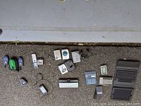 Multiple vintage electronic gadgets arranged on pavement including Walkman players, film camera, calculators, and other devices.