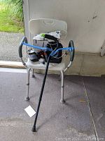 Overview photo showing white plastic shower seat with armrests, black walking cane with ergonomic handle, and multiple medical devices including blood pressure cuffs and cold compress packs placed on the shower seat.