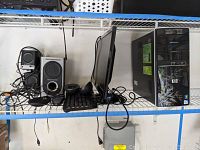 Full setup on shelf including HP desktop tower, Lenovo monitor, Logitech keyboard and mouse, and speakers