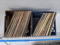 Two plastic crates filled with many LP vinyl records viewed from above, showing a variety of album covers and spines.