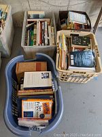 Plastic baskets and containers filled with assorted hardcover and softcover books of various genres, mainly nonfiction and fiction.