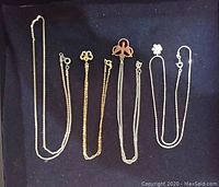 Four silver tone chains laid out side by side on a dark surface showing different designs and clasp styles.