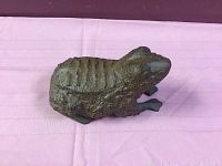 Top-down view of cast iron frog doorstop showing textured back and limbs lying on a pink fabric surface