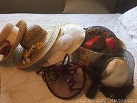 Six vintage ladies hats on a bed including straw and fabric designs, floral and ribbon details visible.