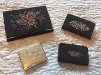 Black evening clutch, floral petit point embroidery, makeup compact, and change purse arranged flat on bed