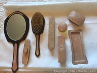 Top view of pink marbled celluloid vanity set including hand mirror, brush, comb holder, boxes, tray, and powder box arranged on white cloth.