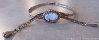 Photo of vintage Hobe gold tone bracelet showcasing the oval genuine shell cameo centerpiece and tassel extension ends on a flat surface.