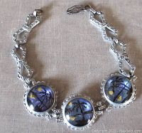 Front view of silver tone butterfly wing link bracelet showing tropical palm tree and moon scene in glass cabochons.