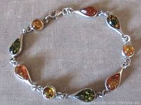 Full view of the sterling silver amber link bracelet laid out showing alternating pear and round shaped amber stones in two colors with lobster clasp marked 925.