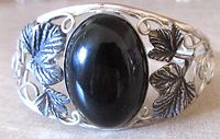 Close-up of silver floral bracelet showing detailed black oval cabochon and darkened leaves design.