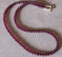 Full view of the garnet bead necklace laid out showing the length and bead color.