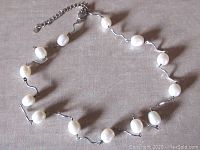 Full view of the necklace laid out showing pearls and silver curved links with lobster clasp and extension chain.