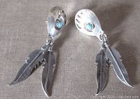 Front view of the pair of earrings showing turquoise stone, bear paw silver top and dual feather dangles
