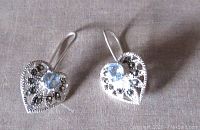 Front view of the pair of earrings showing the heart-shaped design with a central blue stone and marcasite stones embedded in the openwork silver.