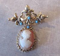 Front view of vintage gold tone brooch showing shell cameo and blue stones