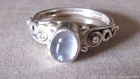 Close-up of front of ring showing oval moonstone and detailed silver ornate band with swirl and bead accents.