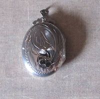 Front view of oval silver photo locket with floral engraving and decorative bail