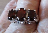 Close-up of ring on finger showing three deep red oval garnet stones set in sterling silver openwork band.