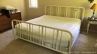 Photo showing the white metal split king bed frame from footboard end with mattress and box springs.