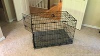 Black metal wire dog crate shown assembled with front door open, placed on carpeted floor in indoor setting.